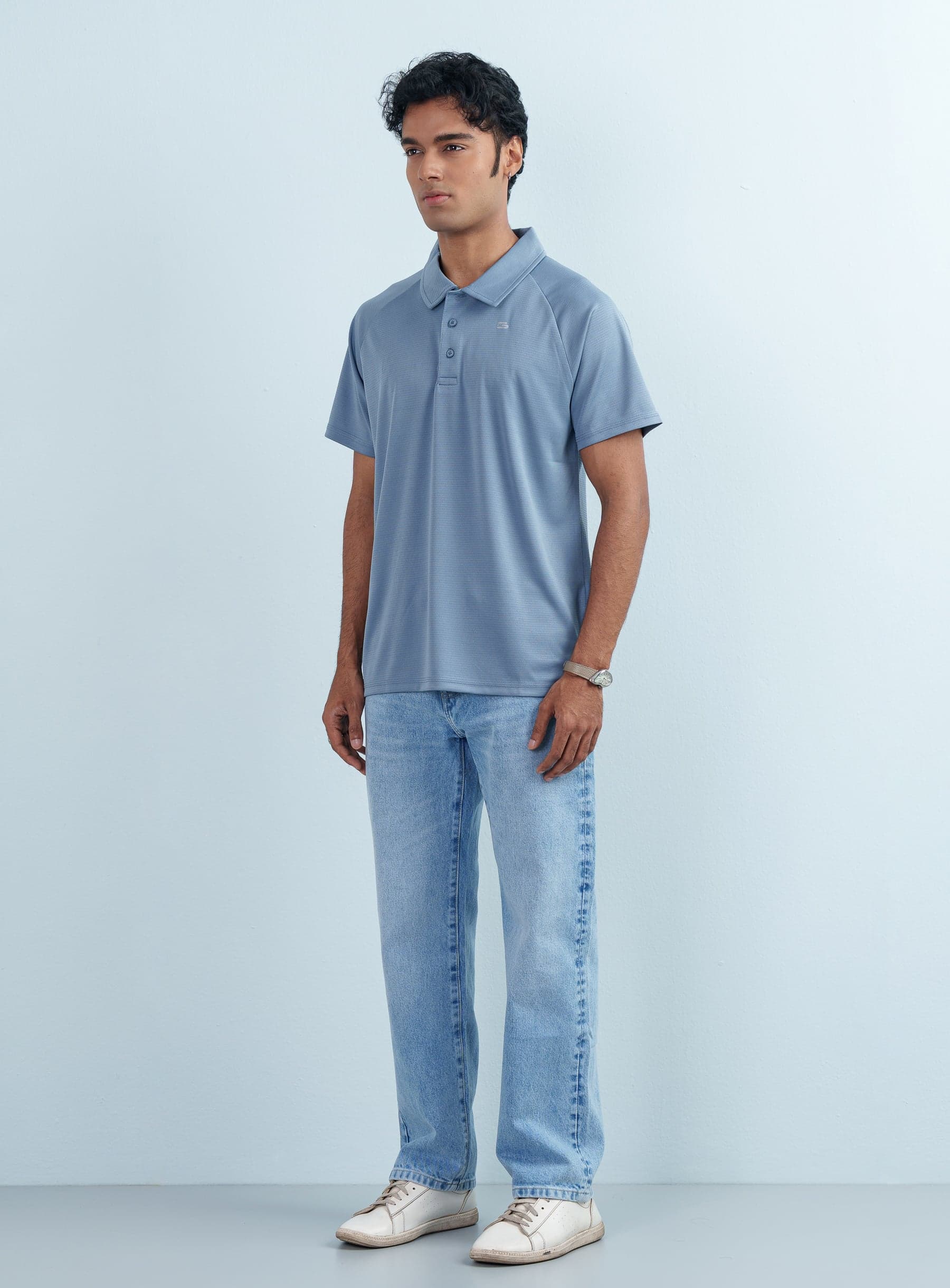Full-length view of a male model wearing the premium Dusty Blue Sports Polo T-Shirt paired with light blue denim jeans and white sneakers.