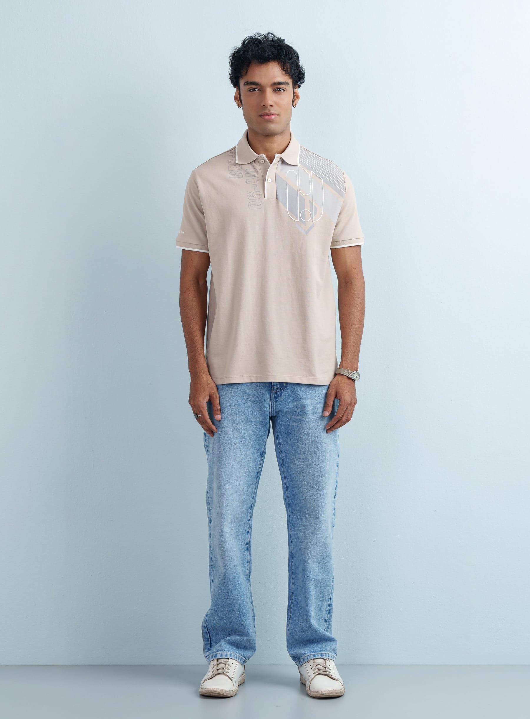 Front view of a male model wearing a men's Beige Graphic Printed Polo Shirt with light blue jeans.