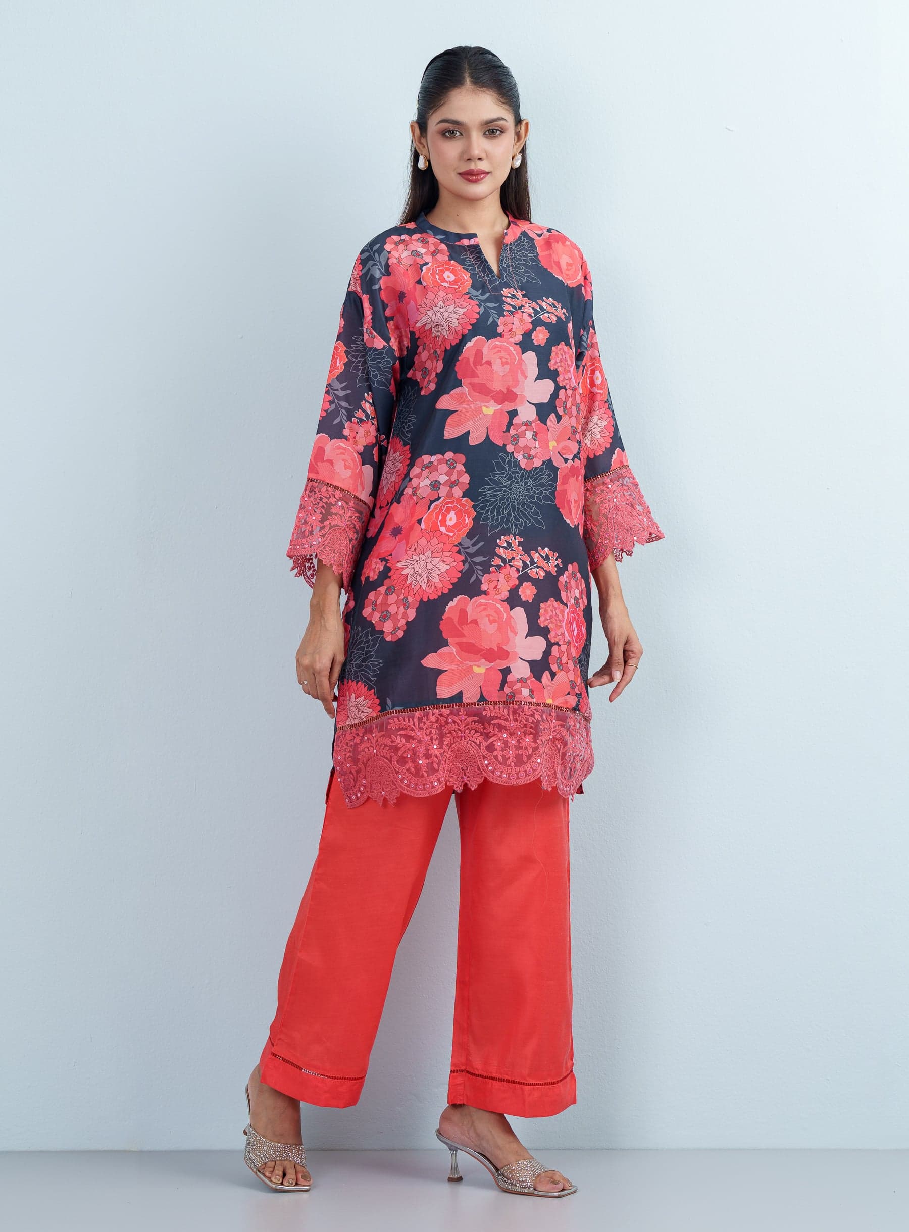 Full body studio pose displaying the elegant drape of a coral wide-leg trouser paired with a floral printed women's two piece top.