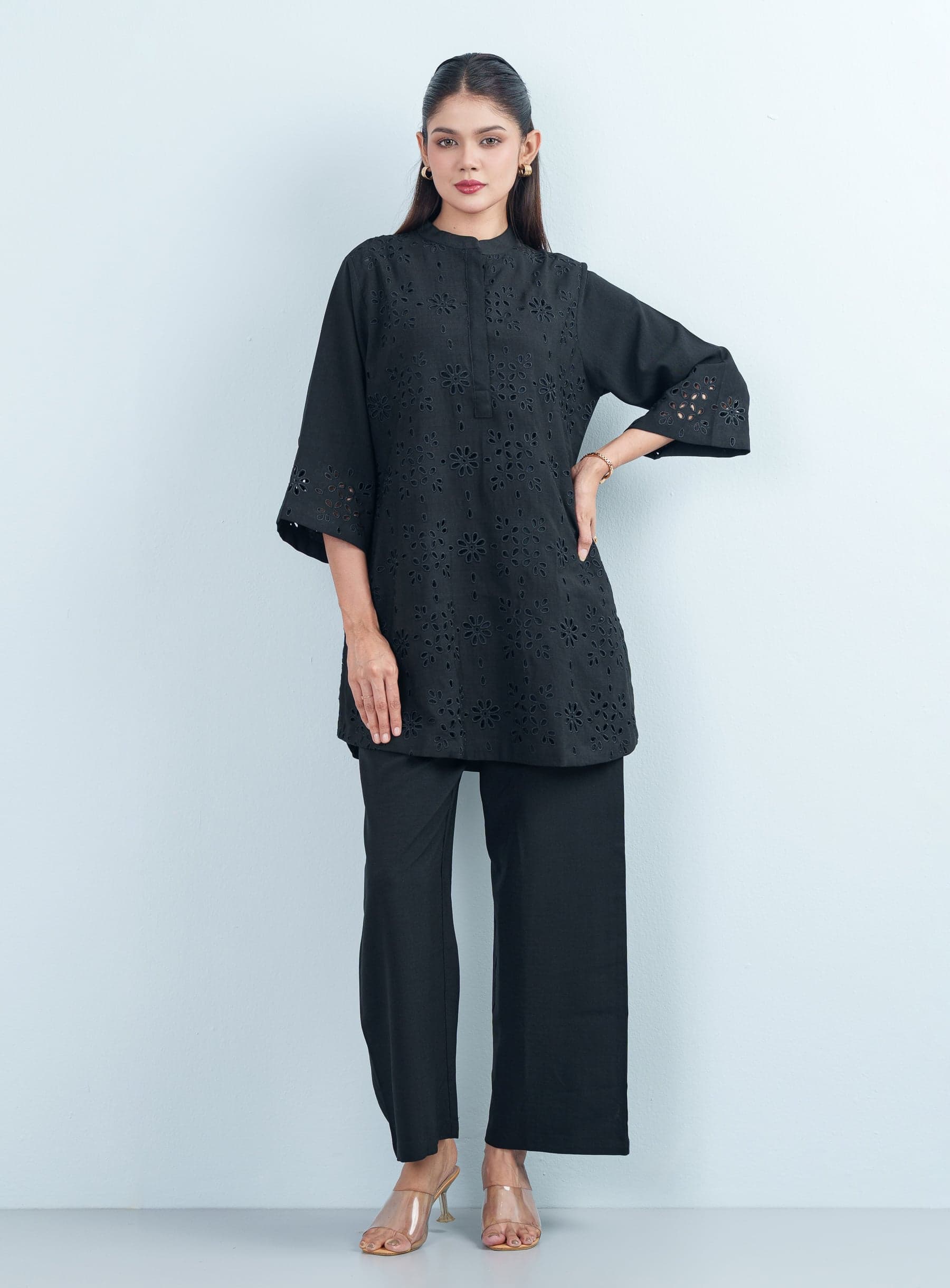 Full-length studio picture of a model wearing a premium black cotton women's two piece set featuring a schiffli embroidered front.