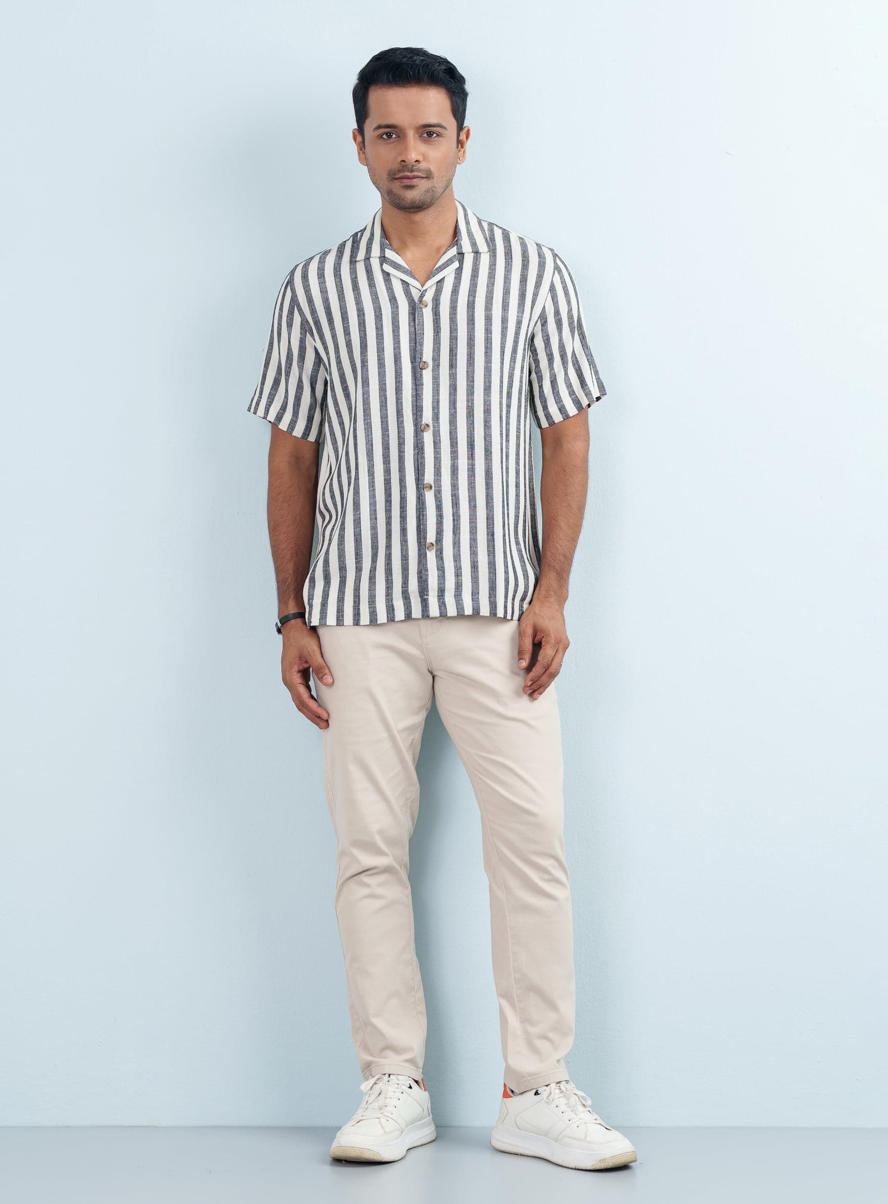Full body shot of a model wearing a men Black Striped Cuban Collar Casual Shirt Half Sleeve paired with beige pants.