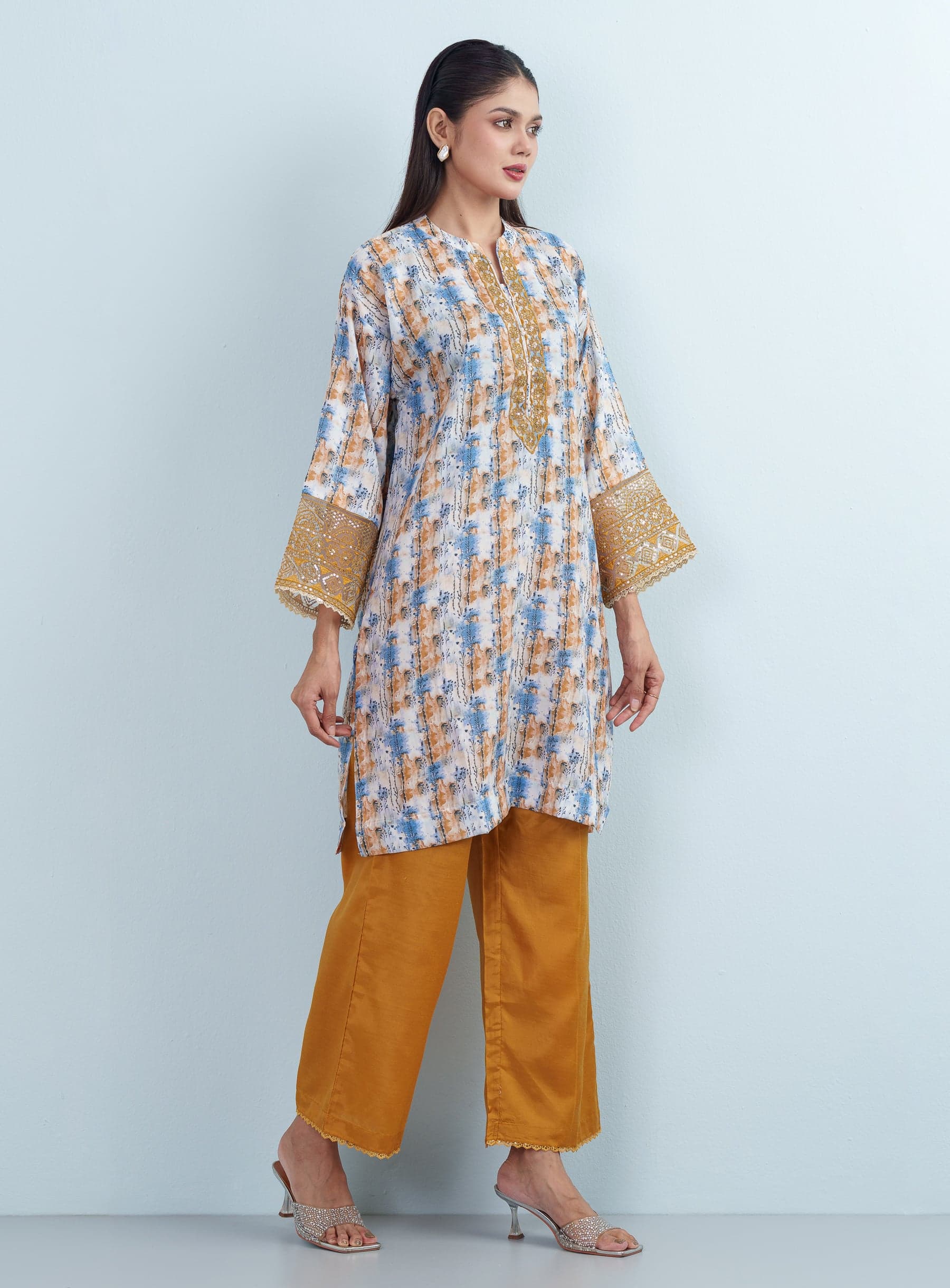 Full-length side view of a model in a mustard and blue abstract printed women's two piece co-ord set with solid wide-leg trousers.