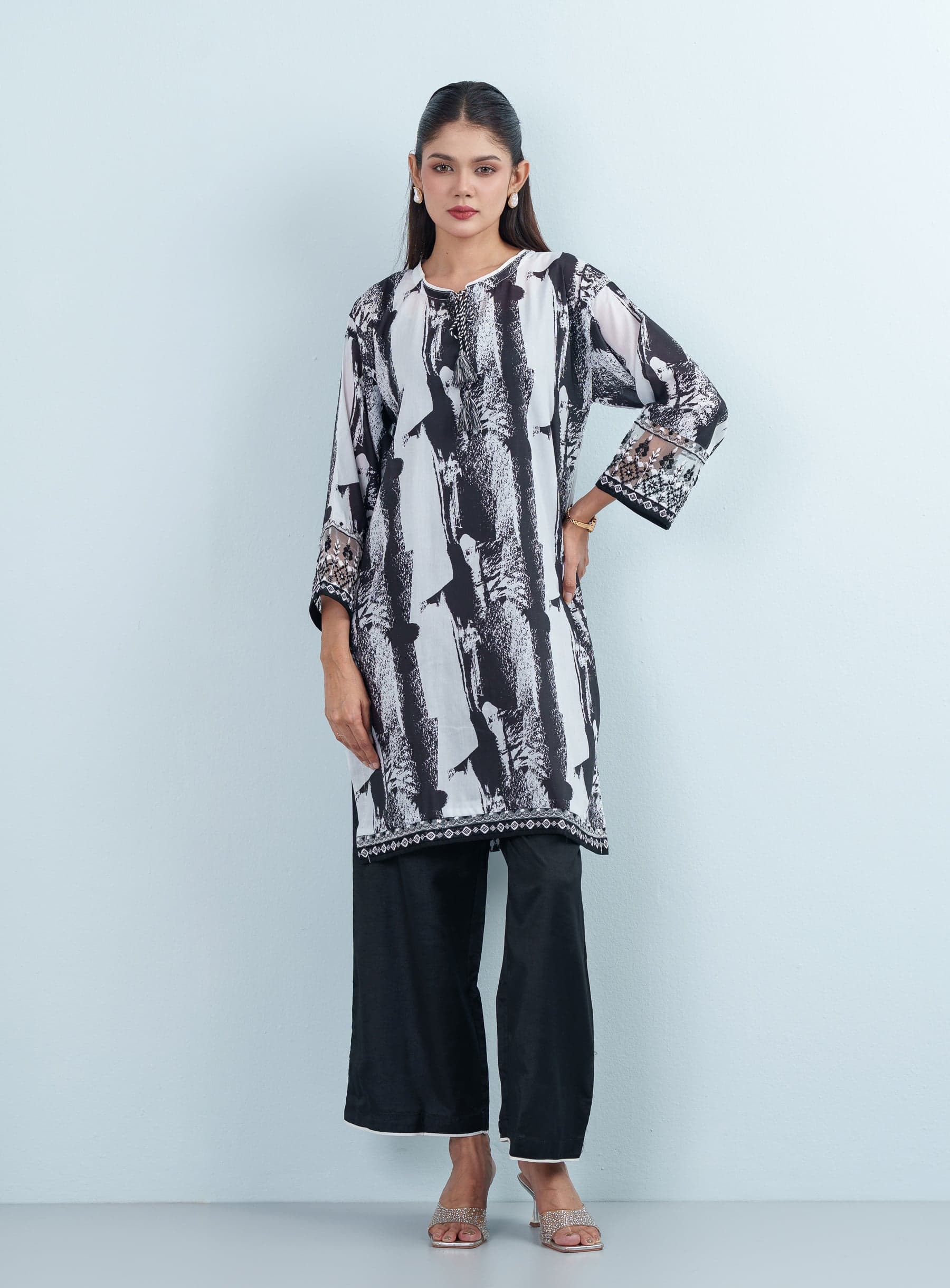 Full-length studio shot of a model wearing an abstract black and white printed cotton women's two piece outfit with solid black wide trousers.