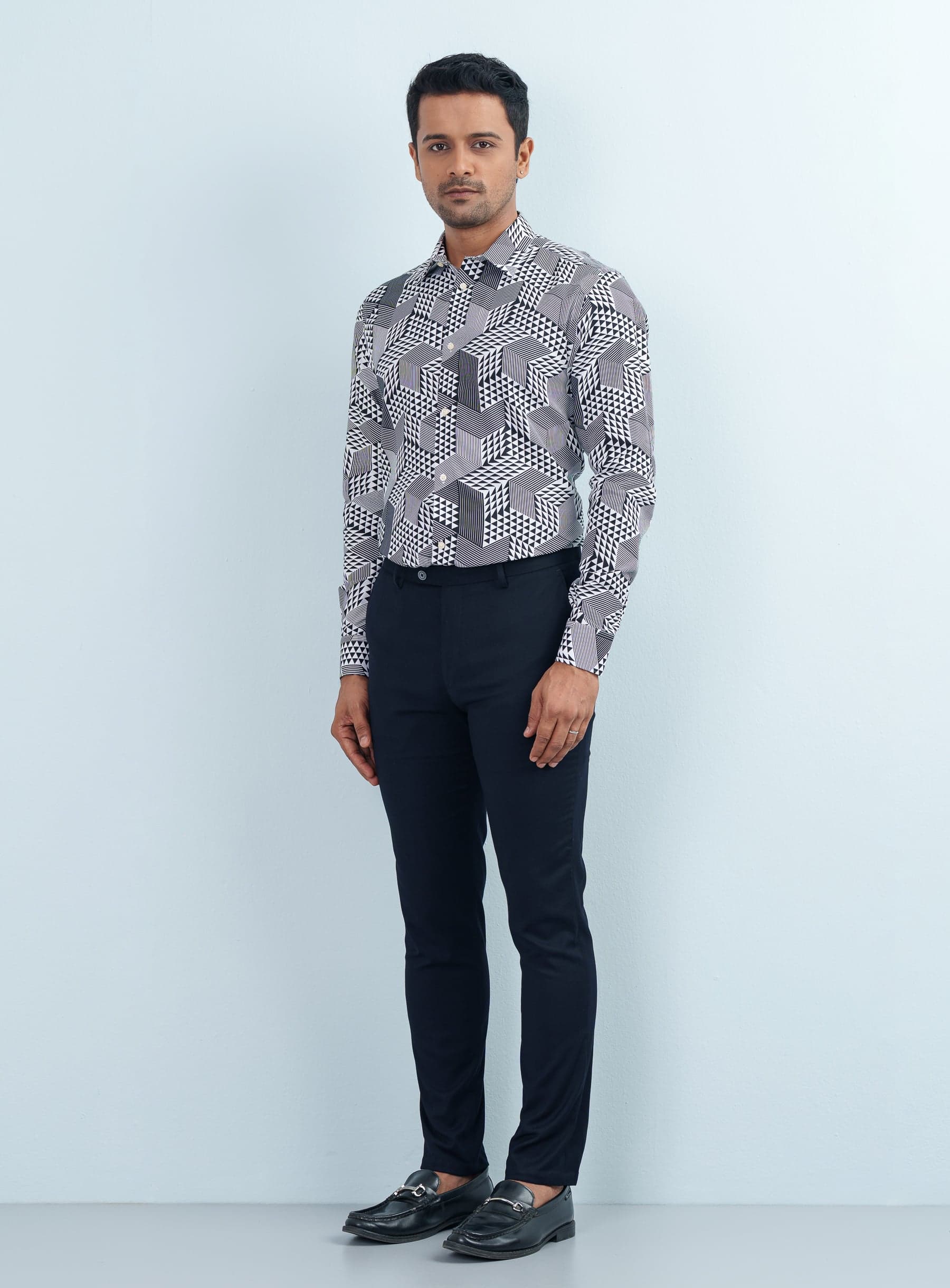 Full-length studio profile view of a model wearing a monochrome triangle pattern formal shirt tucked into black trousers