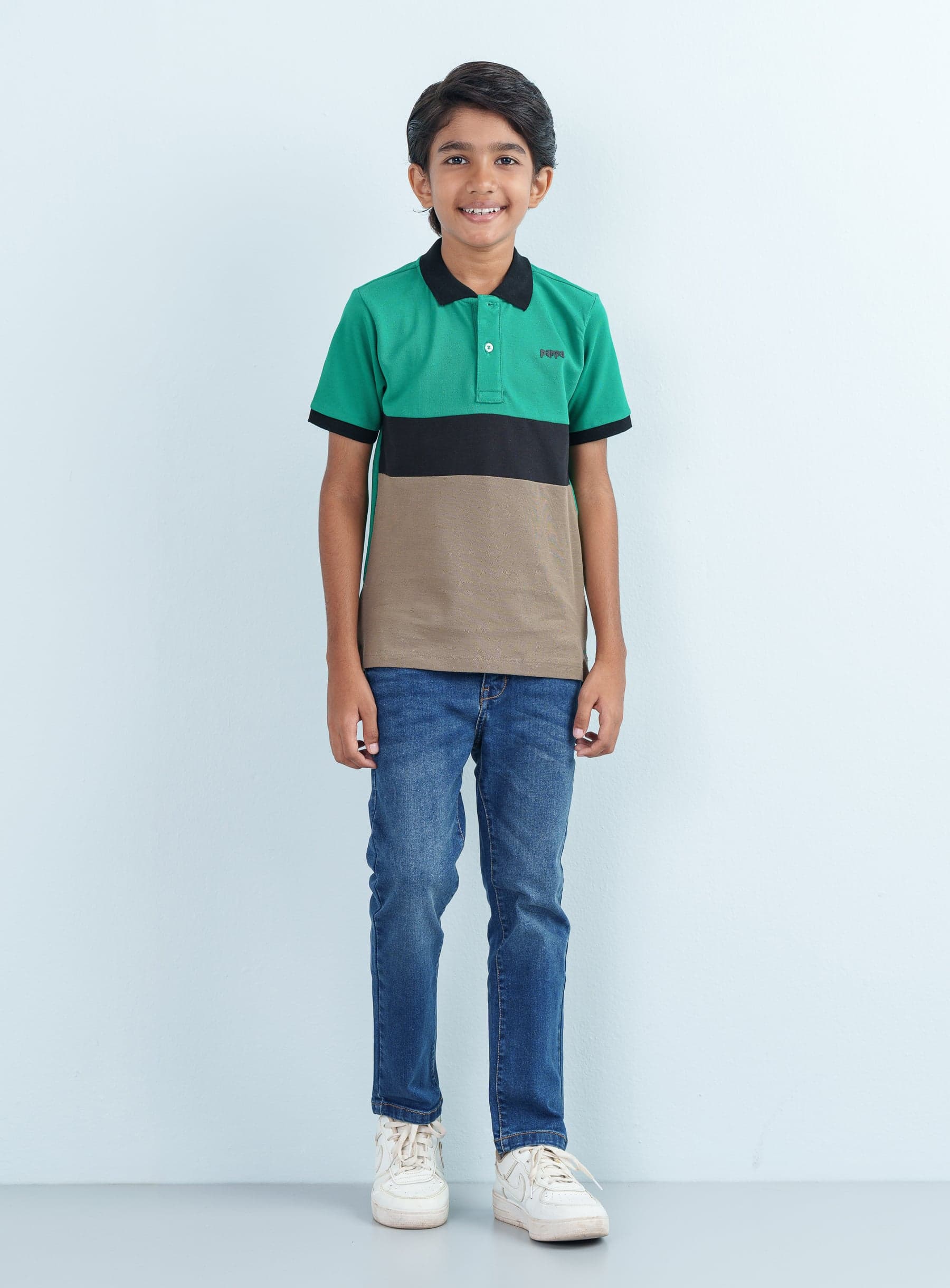 Full-length front shot of a young boy modeling a green color block Polo Half paired with blue denim jeans and white sneakers.